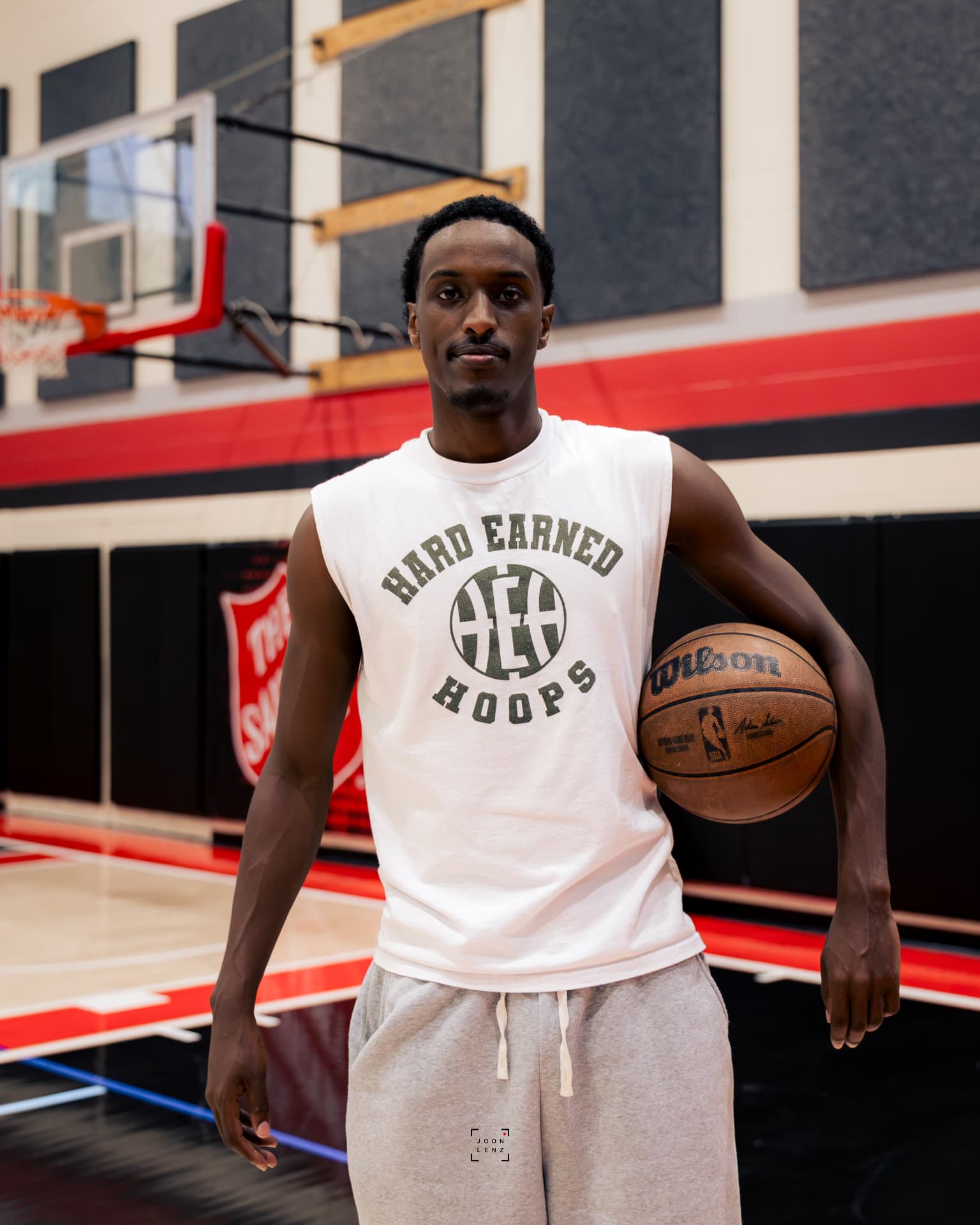Abdullahi Mohamed standing on a gym court in a Hard Earned Hoops shirt with a basketball under his arm.