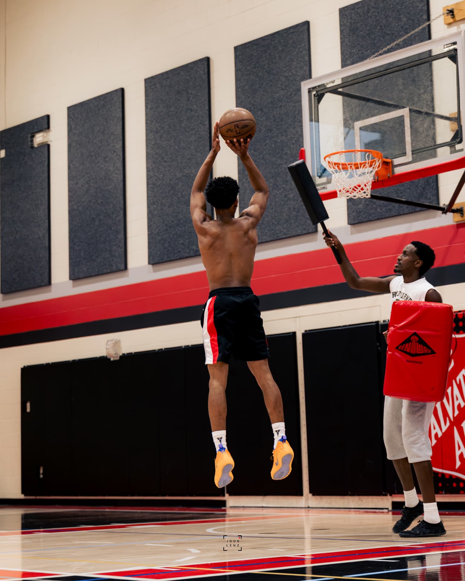 An athlete shooting over a coach holding a contest pad beneath the rim.